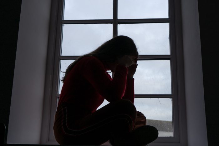 Distressed worker struggling with pressures sits in a window sill